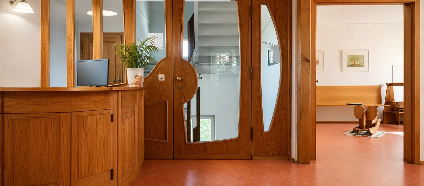 Empfangstresen aus Kiefernholz mit Blick durch die geschwungene Glastür ins Treppenhaus.
