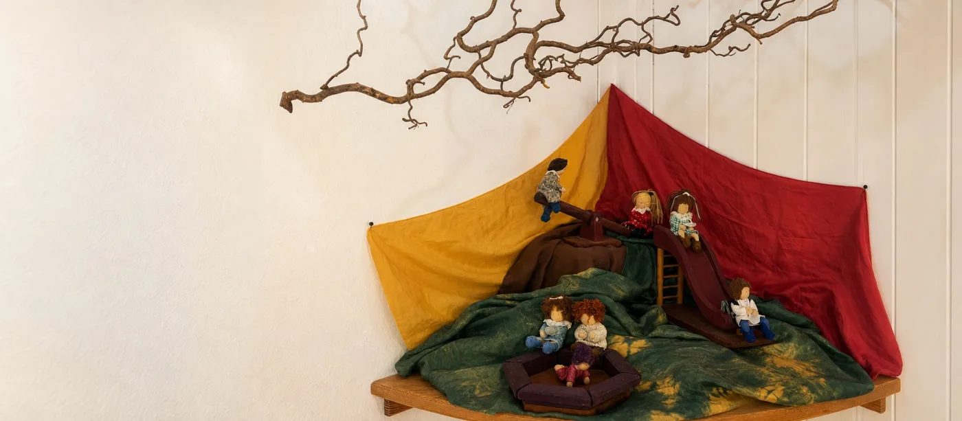 Jahreszeitentisch mit gelben und roten Filztüchern und kleinen Figuren unter einem Zweig.